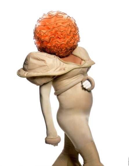 Leigh Bowery in tight cream outfit with orange frilled ball obscuring his face and head, 1989