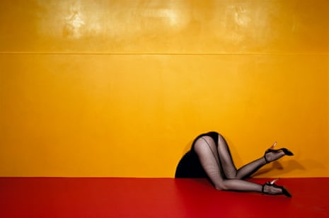A woman’s bottom and legs, in black fishnet tights and high heels, bending over so her top half is missing, against red and yellow background, 1979