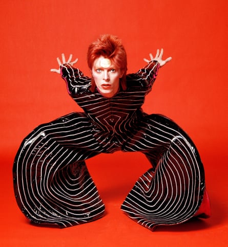 David Bowie wearing black and white striped outfit by Japanese designer Kansai Yamamoto, against red background, 1973